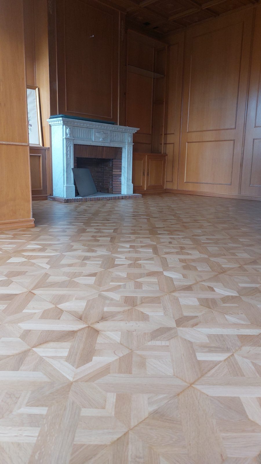 Parquet de mosaico geométrico restaurado en un salón con chimenea por Solparquet en Lleida